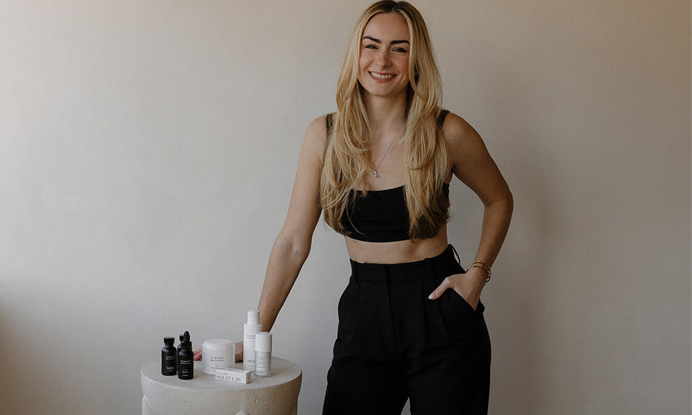 Evara CEO standing next to a white pedestal with Vivant skincare products against a plain wall.